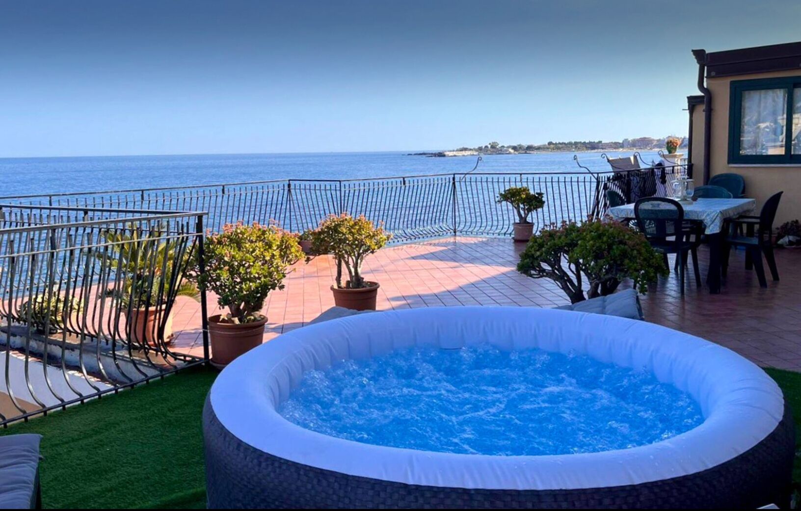 Una terrazza sul tetto con una vasca idromassaggio, piante in vaso e vista sul mare.