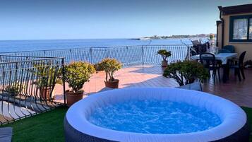 Una terrazza sul tetto con una vasca idromassaggio, piante in vaso e vista sul mare.