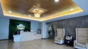 A spacious lobby with a reception desk, two plush armchairs, a chandelier, and a green wall with a neon sign.