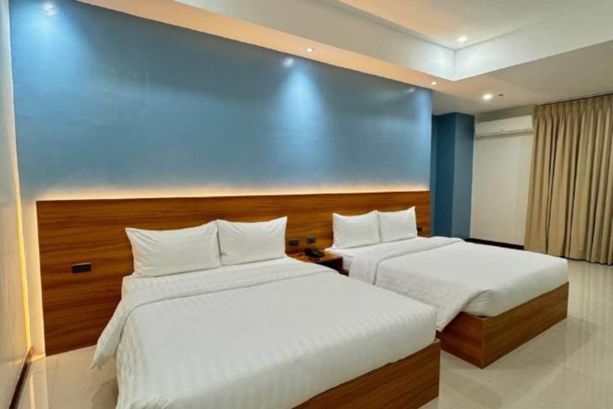 Een hotelkamer met twee bedden, houten hoofdeinden en een groot raam met gordijnen.