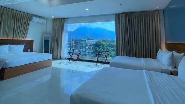 A modern hotel room with two beds, a large window with a mountain view, and a balcony with a table and chairs.