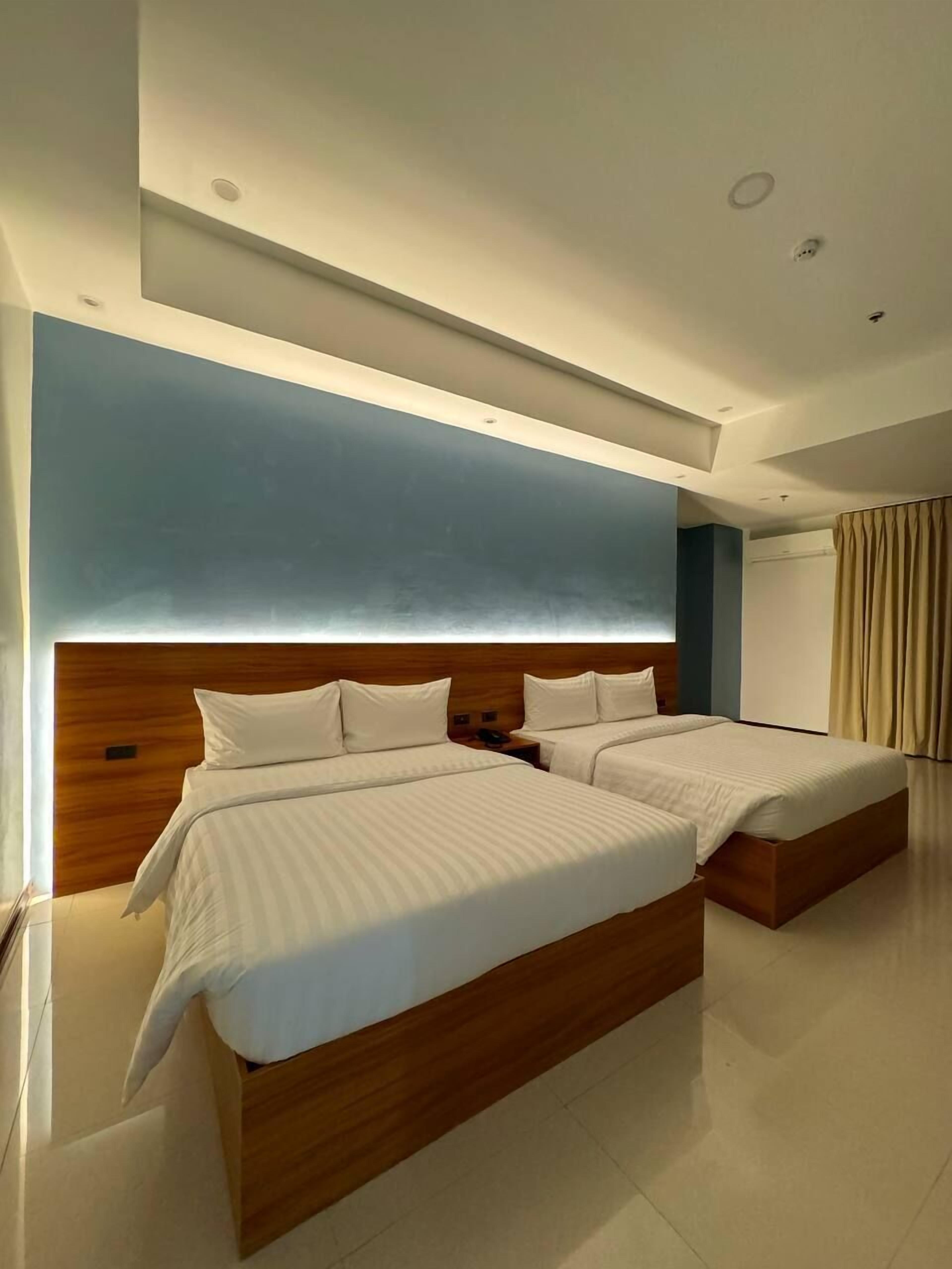 A modern hotel room with two beds, a wooden headboard, and a large window with curtains.