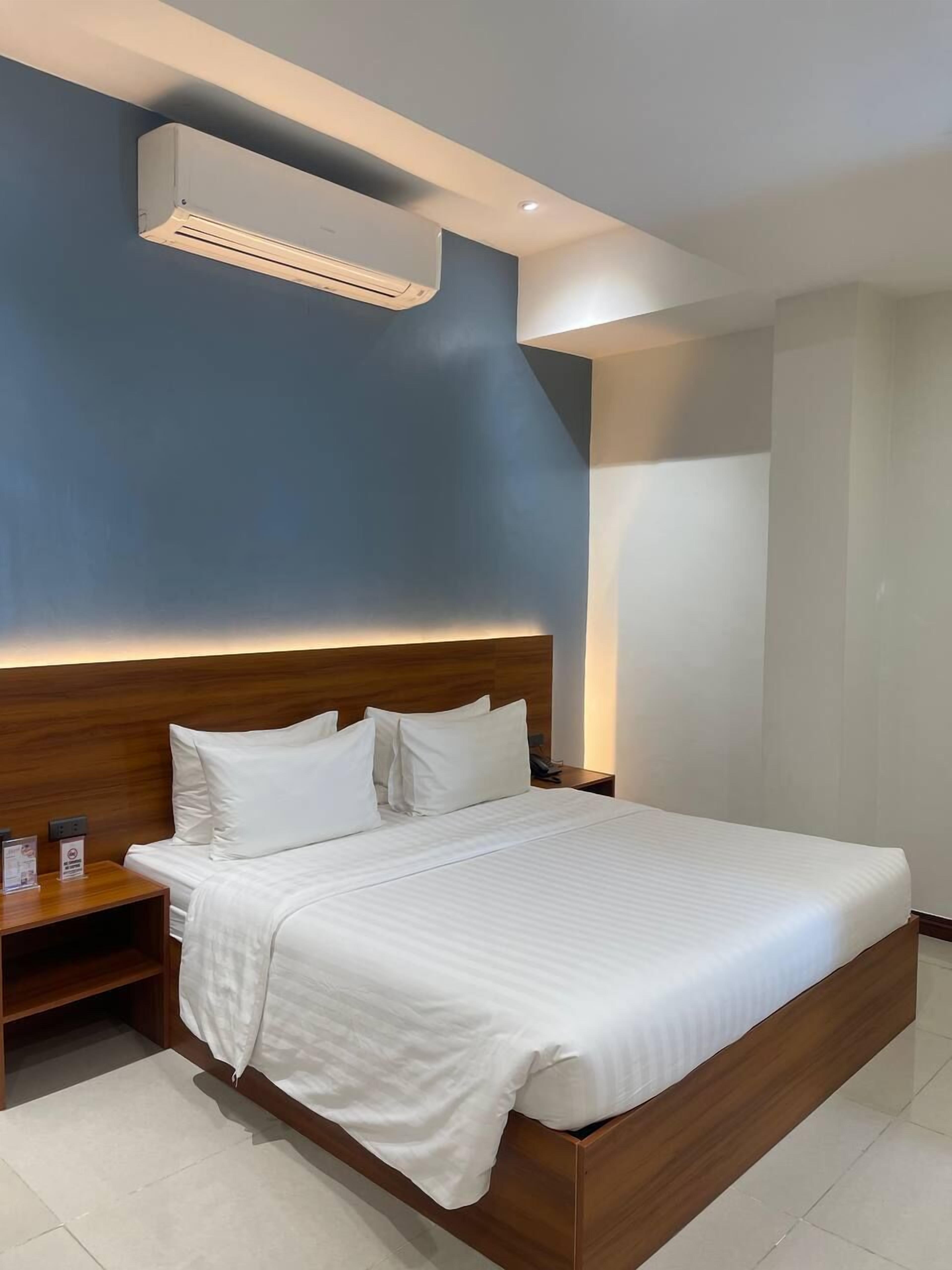Ein modernes Hotelzimmer mit einem großen Bett, einem hölzernen Kopfteil und einer fest installierten Klimaanlage.