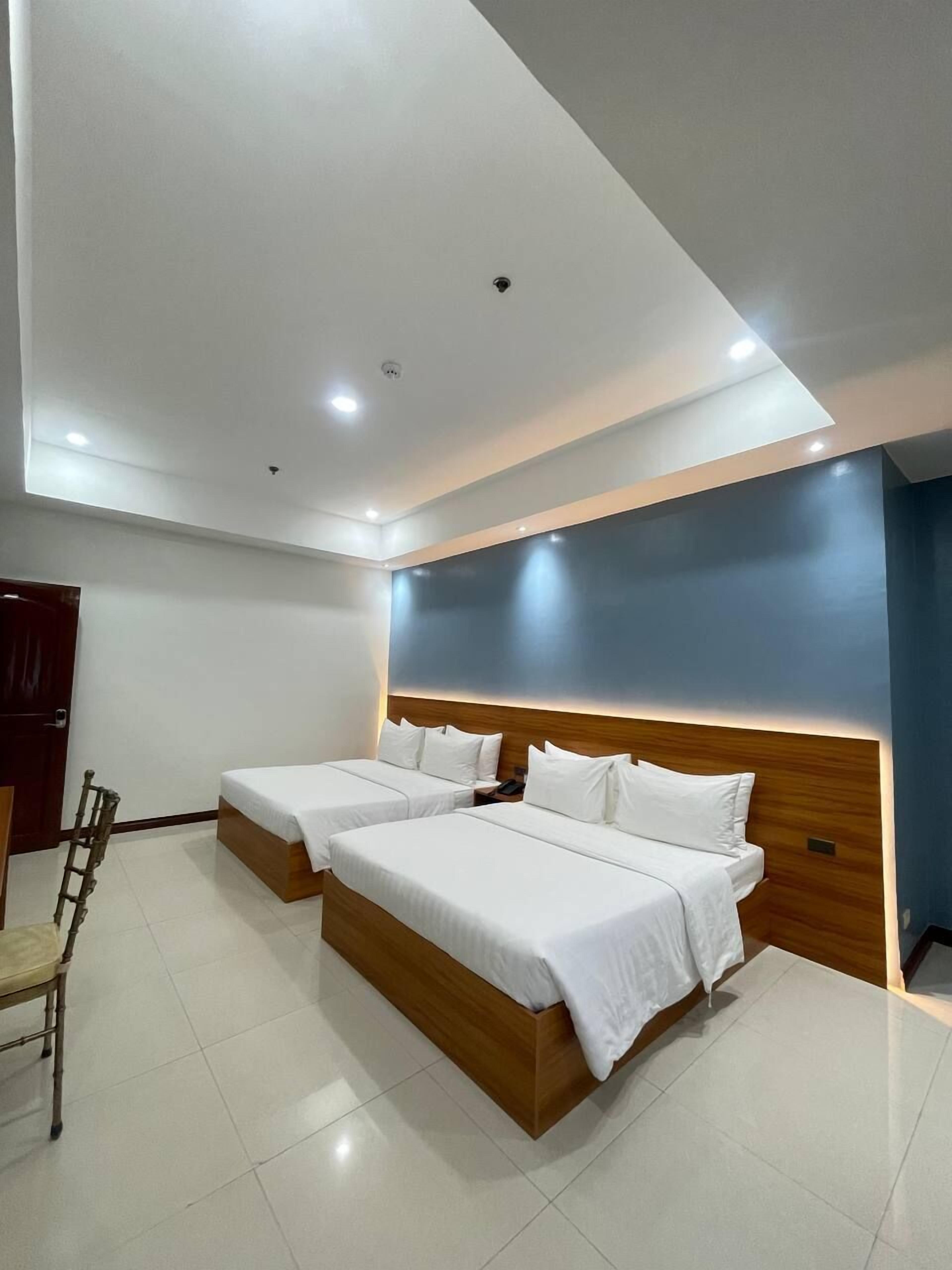 A modern hotel room with two single beds, a wooden headboard, a small desk, and a chair.