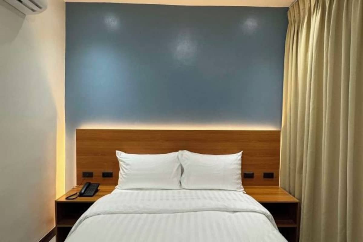 Een hotelkamer met een bed, een houten hoofdbord, een nachtkastje met een telefoon en een gordijn.