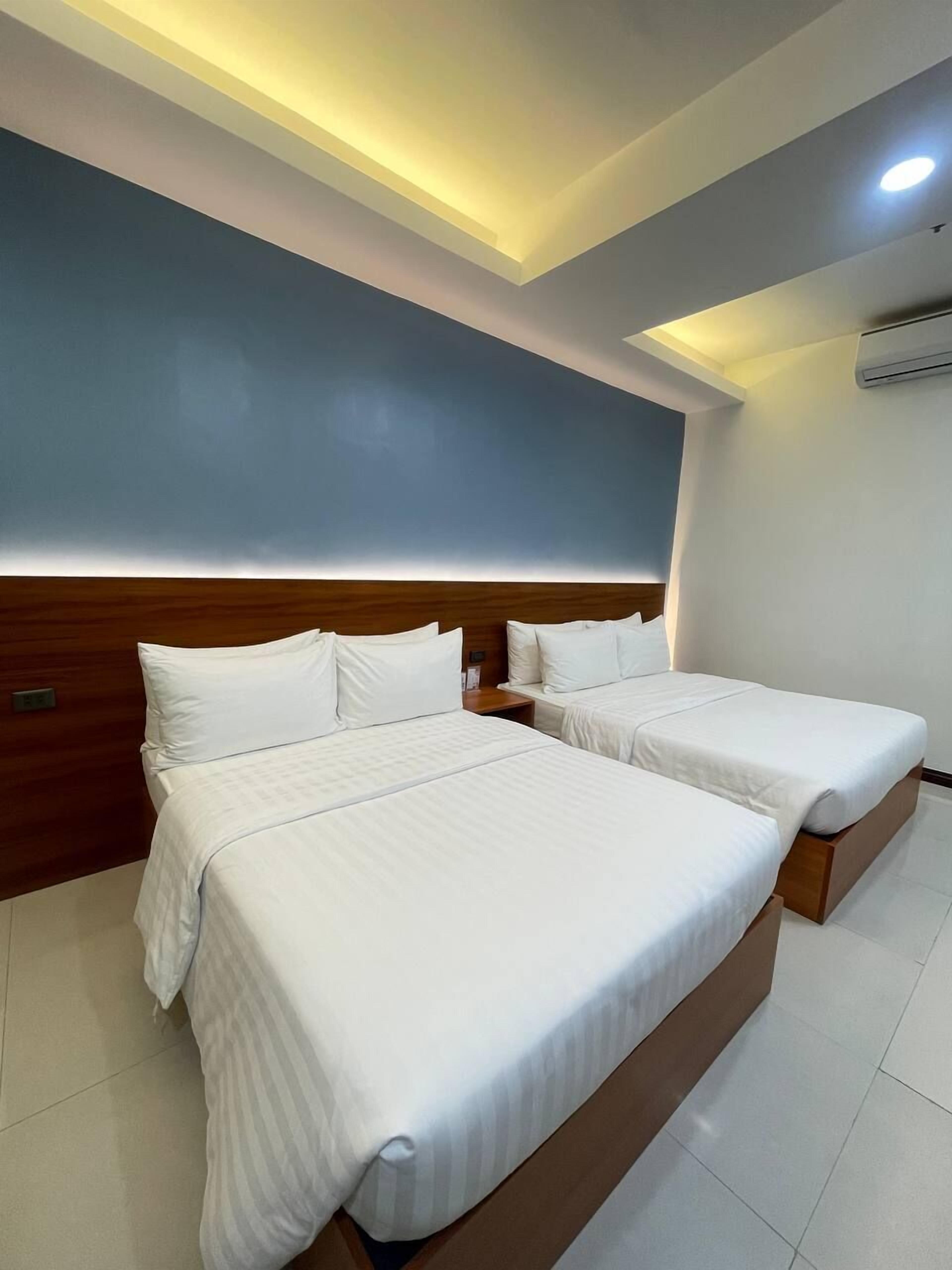 Habitación de hotel con una cama grande, una cama más pequeña y un cabecero de madera.