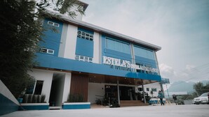 A two-story hotel with a blue and white facade, a visible entrance, and a sign that reads "ESTELA'S HOTEL".