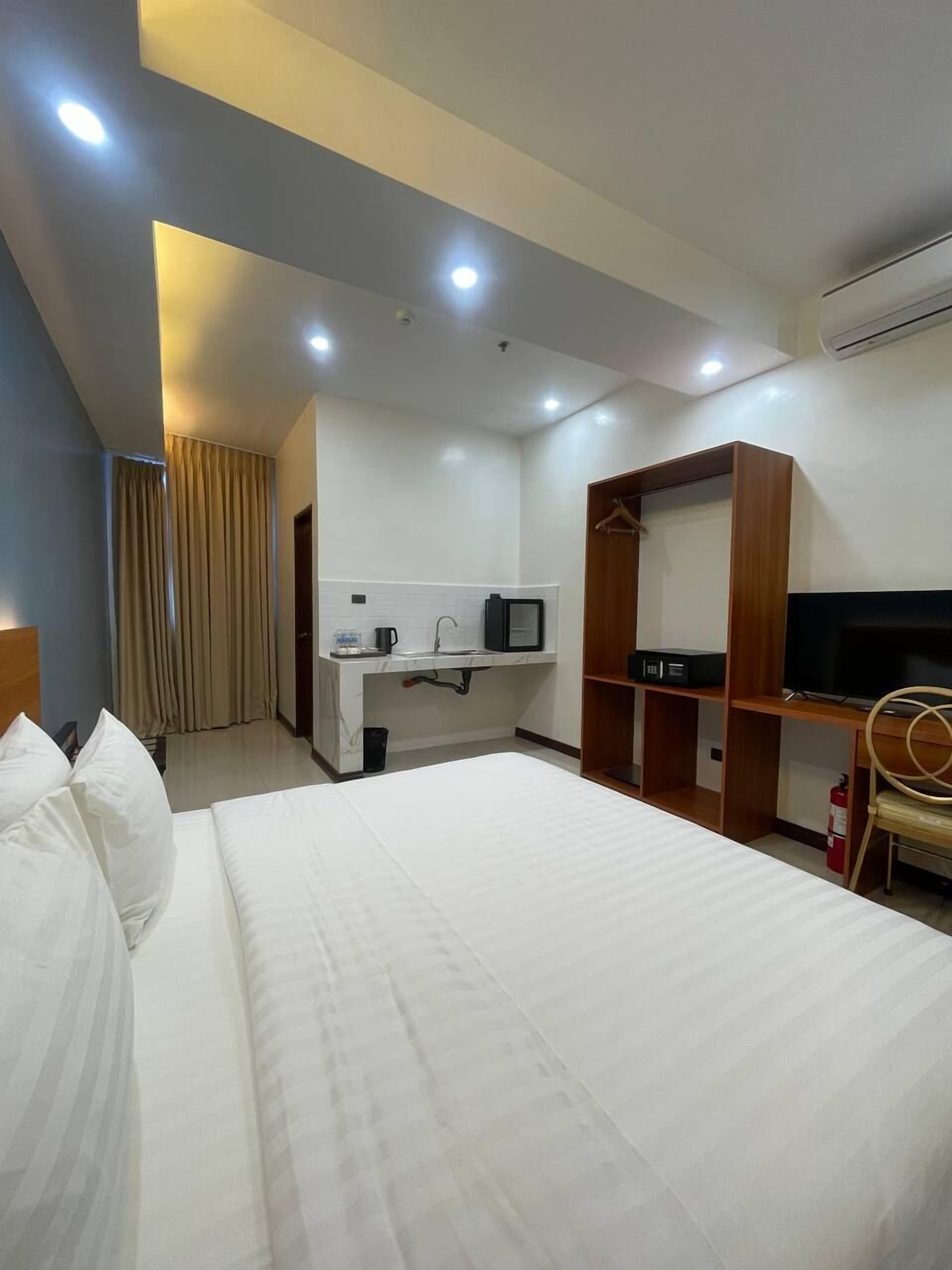 Une chambre d’hôtel avec un grand lit, un bureau avec un ordinateur, une télévision et une armoire.