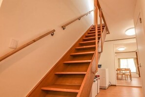 Un escalier en bois avec des rampes, un réfrigérateur blanc et un coin repas avec des chaises.