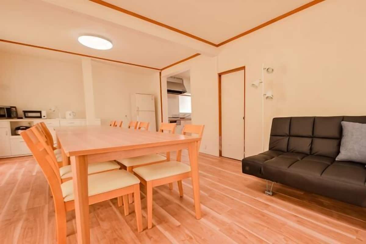 Een eethoek met een houten tafel en stoelen, een bank en een keuken op de achtergrond.
