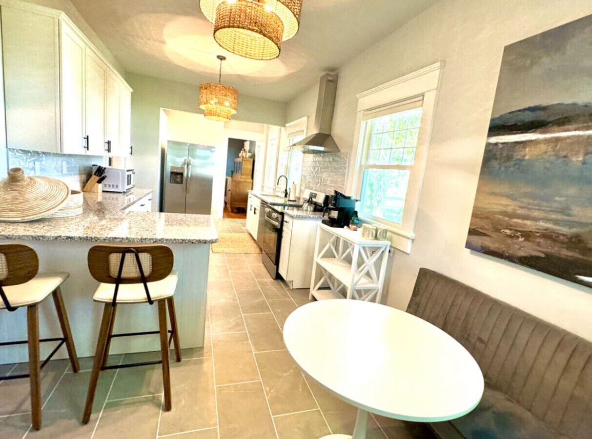 Una cocina moderna con una isla central, taburetes de bar, una mesa redonda y un banco.