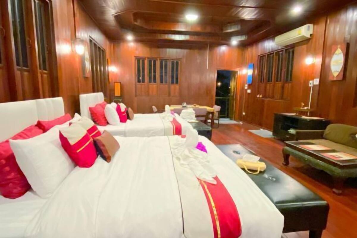 A hotel room with wooden paneling, two beds with red and white bedding, a small table, a sofa, and a television.