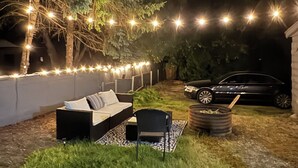 An outdoor seating area with a sofa and chairs, a car parked nearby, and string lights in the background. - Historic Vintage House Downtown Grand Rapids  (Grand Rapids)