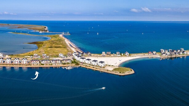 Vista aérea de un pueblo costero con un puerto deportivo, playa de arena y edificios residenciales.