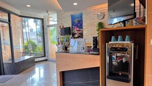 Un'area reception di un hotel con un bancone in legno, una sveglia digitale, una macchina per il caffè e un televisore montato a parete.