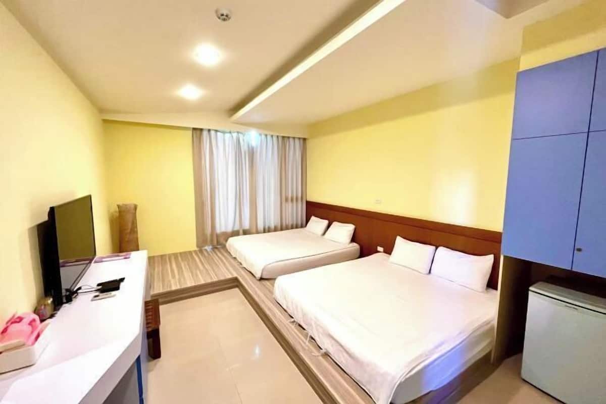 A hotel room with two beds, a desk with a computer, and a television.