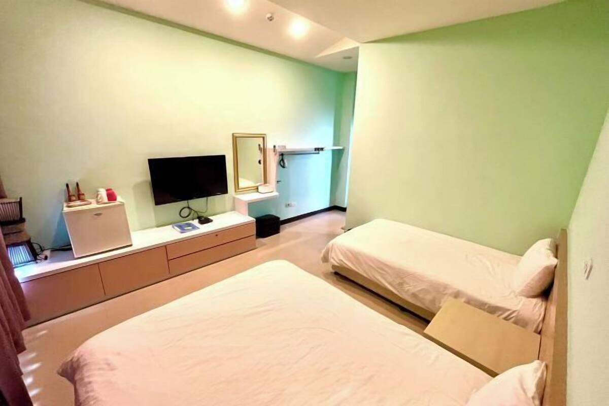 A hotel room with two beds, a TV, a desk with a computer, and a mirror.
