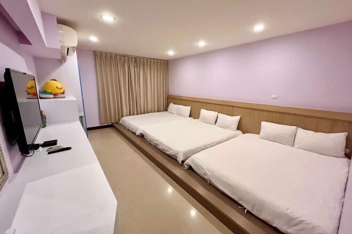 A hotel room with two beds, a flat-screen TV, a mirror, a window with curtains, and a wall-mounted air conditioner.