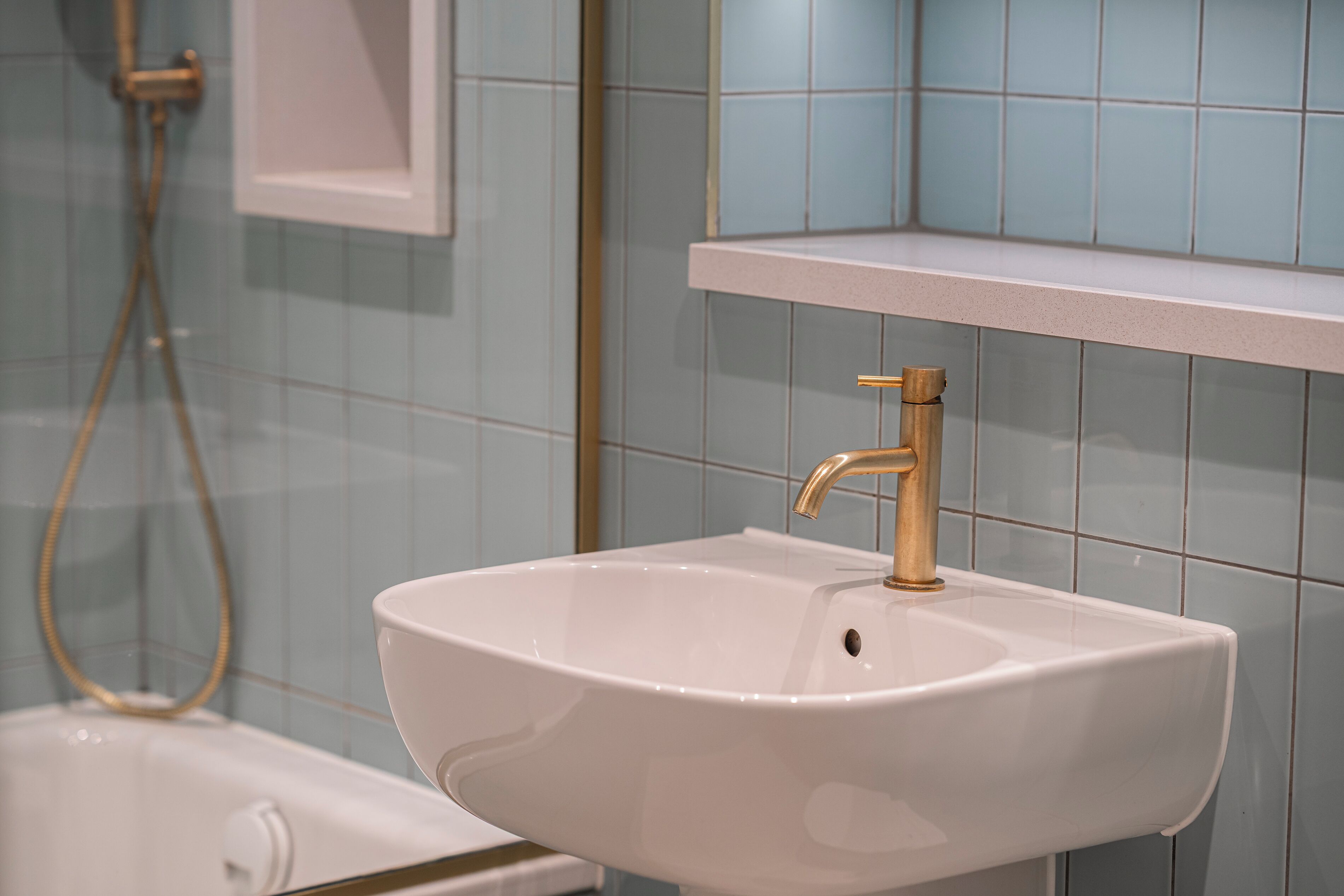Une salle de bain avec un lavabo blanc, un robinet doré et un espace douche.