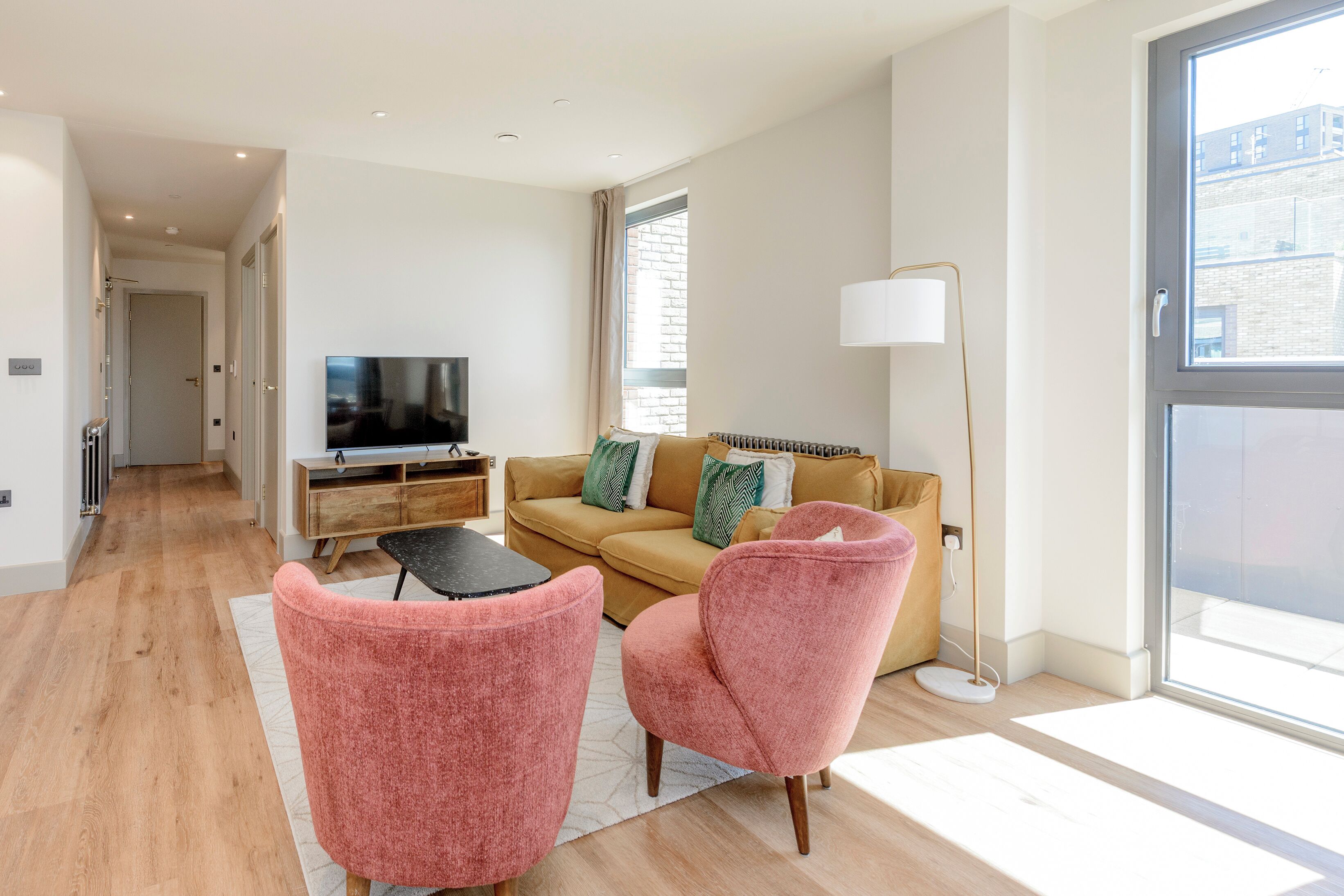 A modern living room with a sofa, two pink chairs, a TV, and a floor lamp.