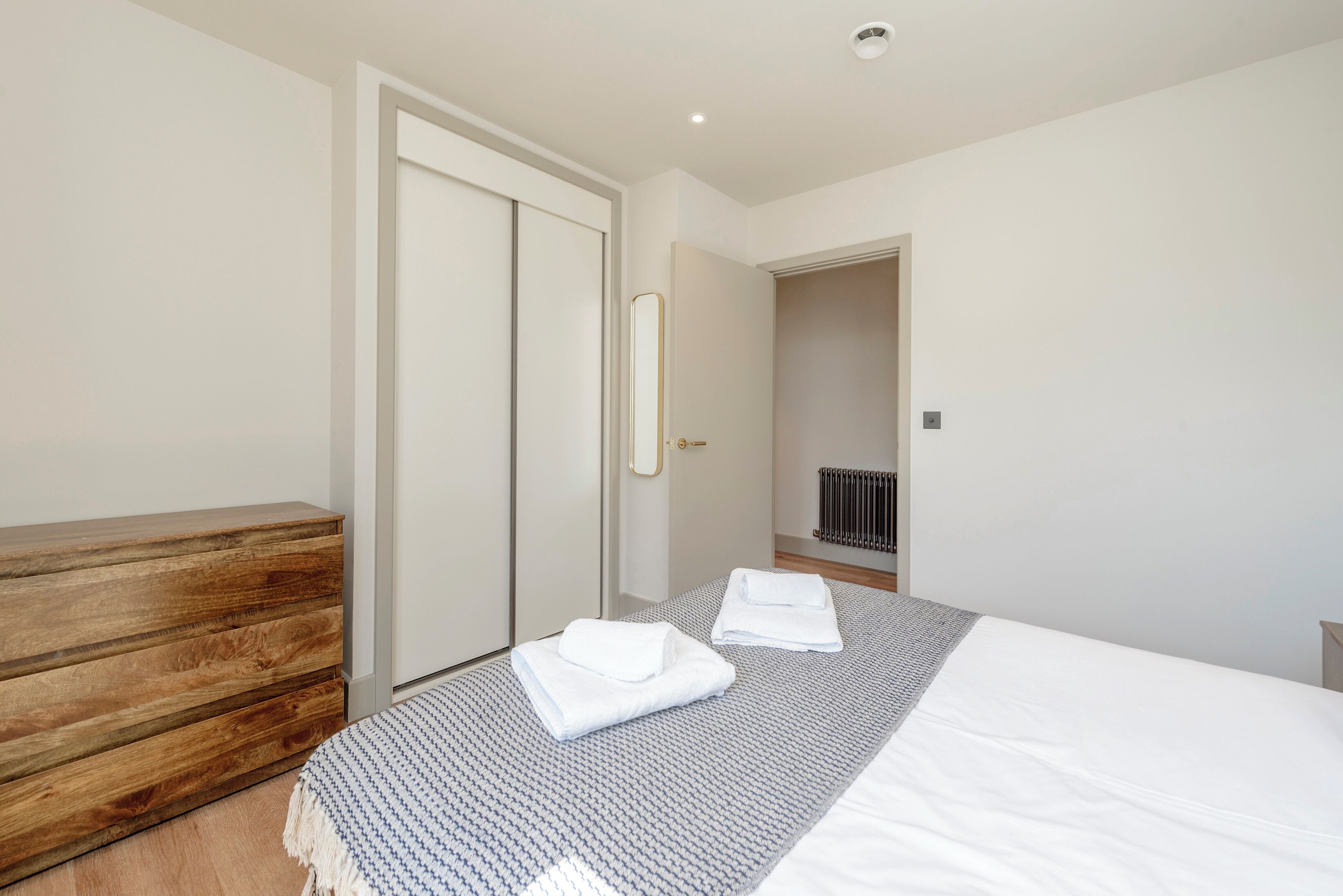 A bedroom with a wooden dresser, a bed with white linens, and a mirror on the wall.