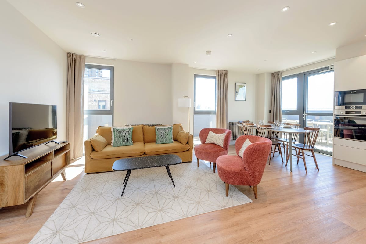 A modern living room with a sofa, chairs, a coffee table, and a TV. There is a dining area with chairs and a table.