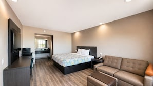 A modern hotel room with a bed, a sofa, a desk, and a TV.