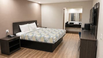 A modern hotel room with a large bed, a desk, a television, and a bathroom with a mirror and sink.