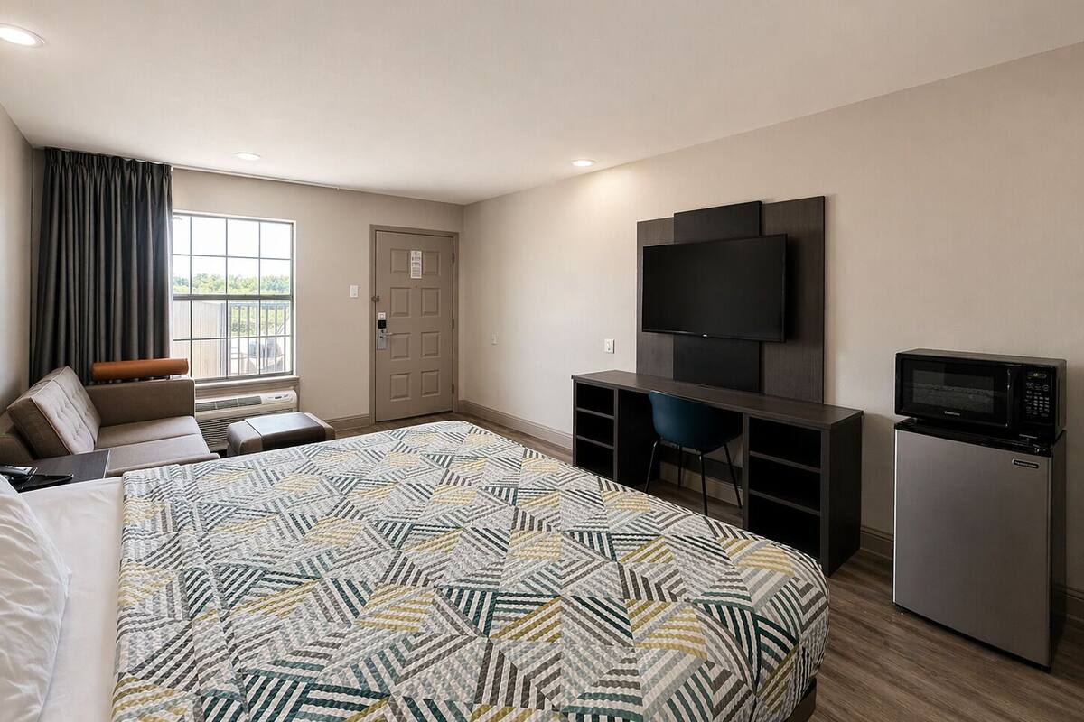 A hotel room with a bed, a desk, a TV, a microwave, and a door.