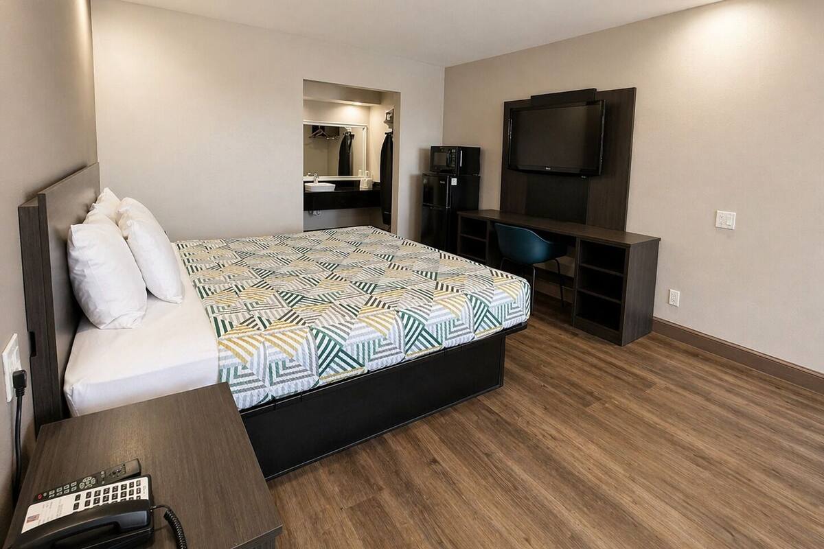 A hotel room with a bed, a desk, a chair, a TV, and a mirror.