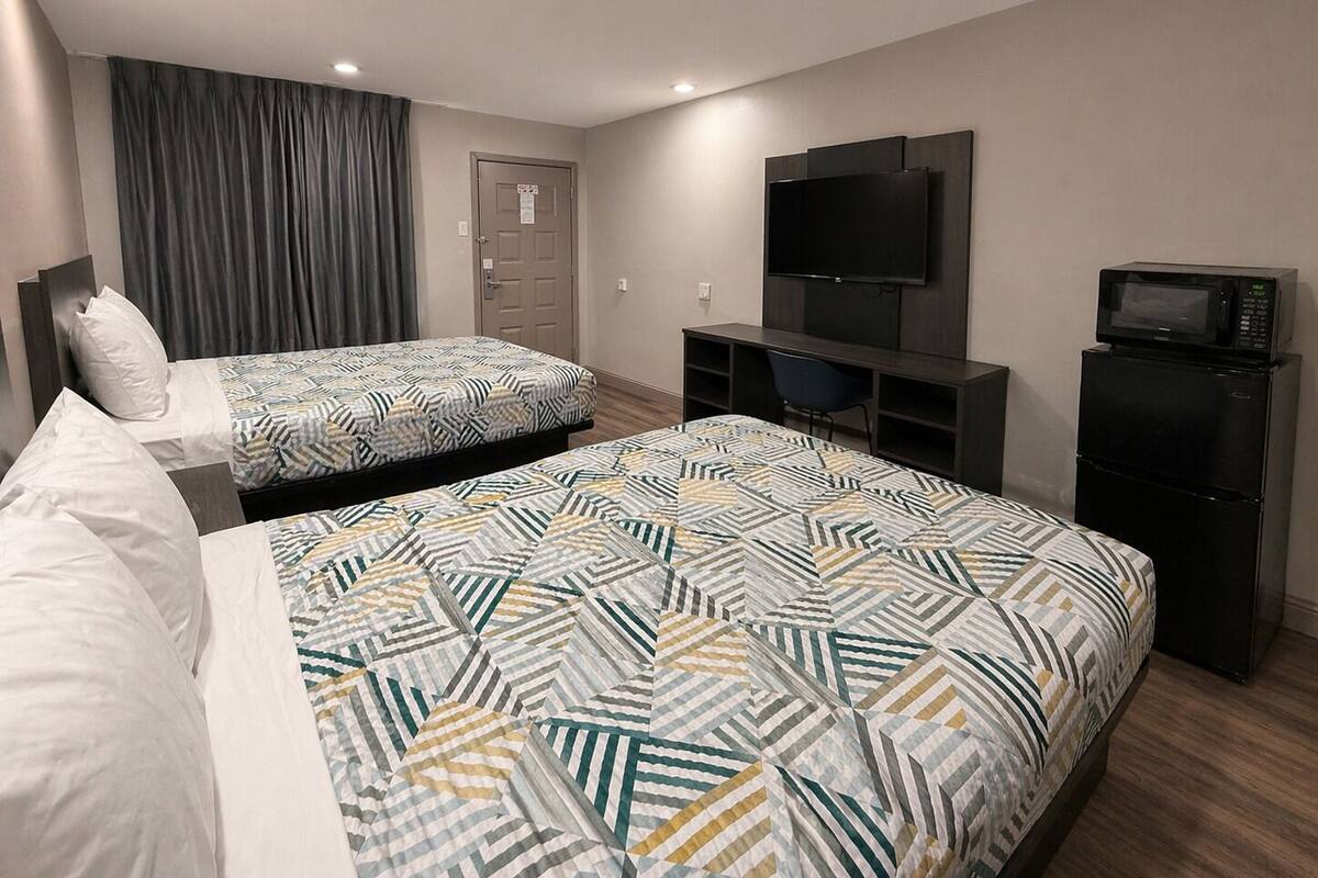 A hotel room with two beds, a TV, a microwave, and a door with a sign.