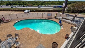 A swimming pool with a fenced deck, lounge chairs, and a view of a highway.