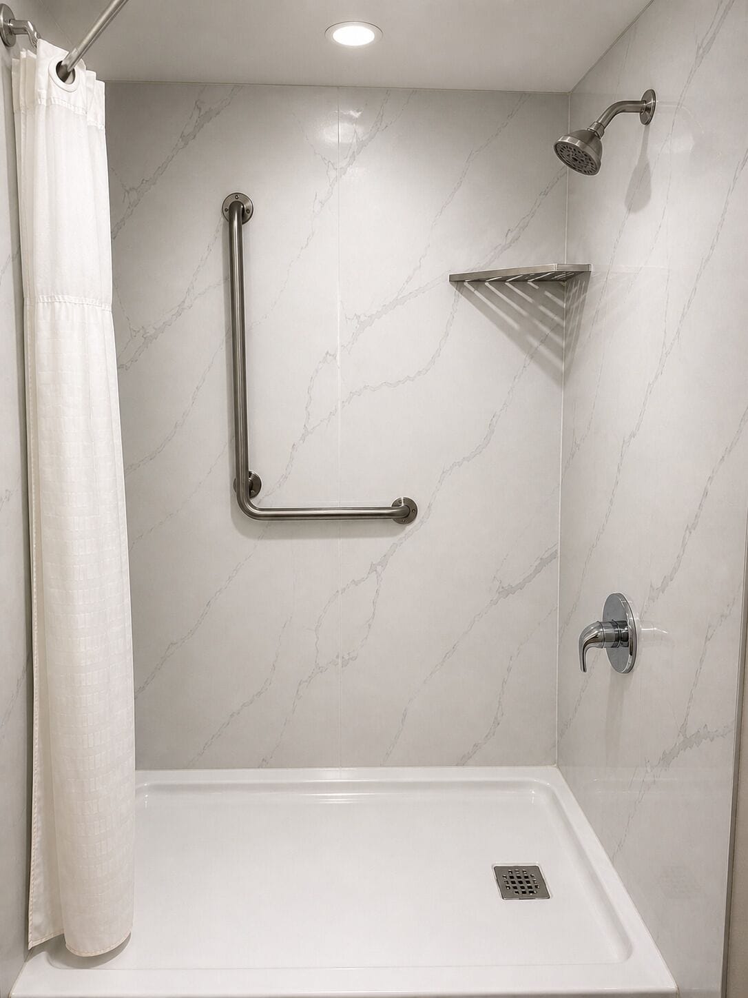 Une douche équipée d’une barre d’appui, d’un pommeau de douche amovible et d’un drain au sol.