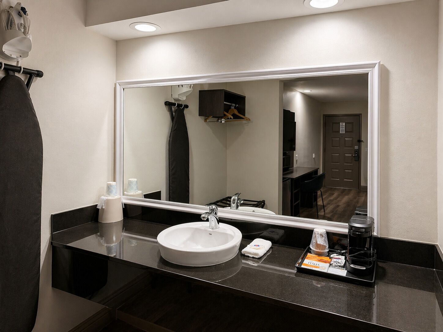 Un baño moderno con un espejo grande, un lavamanos y una cafetera sobre la encimera.