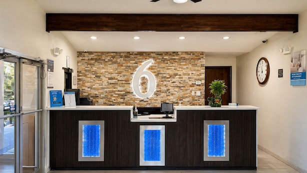 A reception desk with a stone wall backdrop, a clock, and a sign indicating a 6-minute wait.