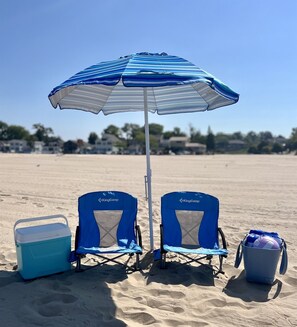 Twee blauwe KingCamp strandstoelen, een blauw-wit gestreepte strandparasol, een blauwe koelbox en een blauwe emmer op een zandstrand.