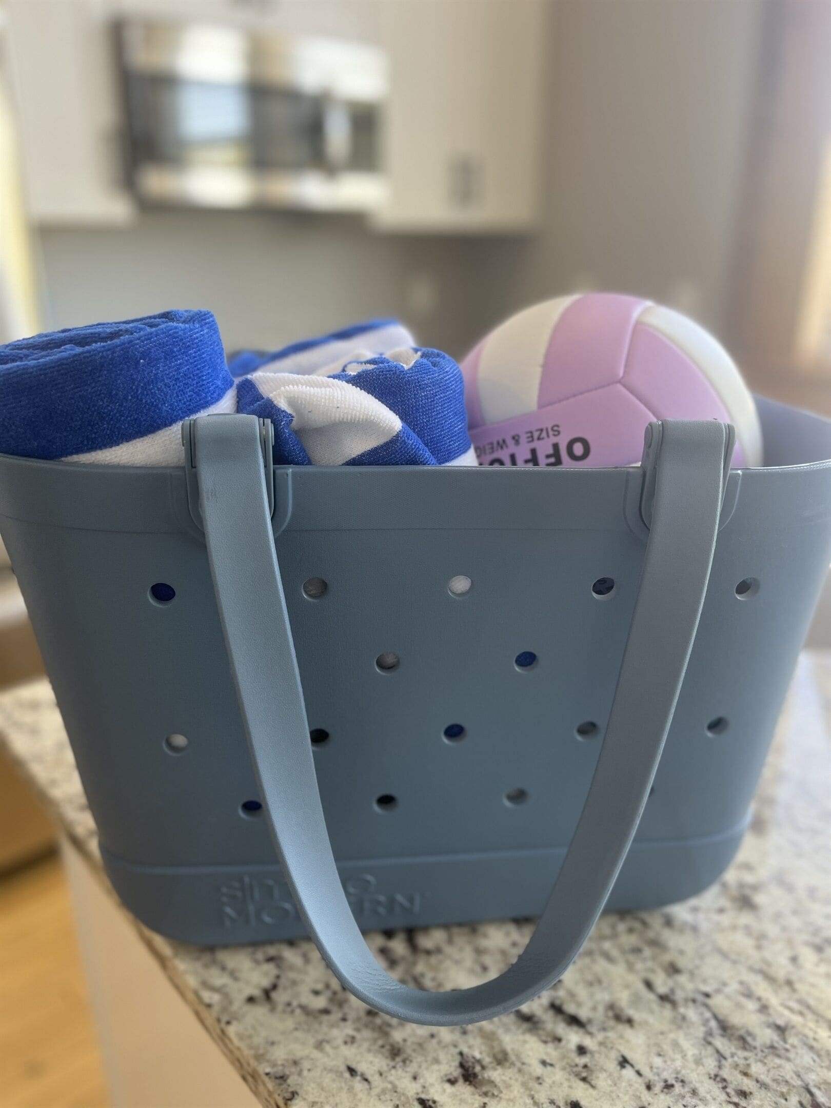 Un sac fourre-tout gris avec une anse, contenant un ballon de volley-ball et un objet bleu et blanc.