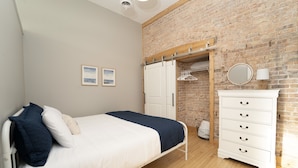 Une chambre à coucher avec un lit, une commode, un miroir et un mur en briques.