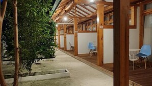 Ein überdachter Außenbereich mit nummerierten Holzwänden, einem Betonboden und einem Baum.