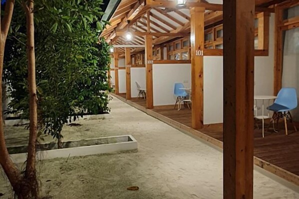 A covered outdoor seating area with numbered wooden partitions, a concrete floor, and a tree. - Origami Inn Himandhoo (Himandhoo)