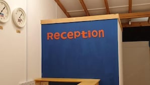 Ein Empfangsbereich mit einem blauen Schild, auf dem 'Reception' steht, und zwei Uhren an der Wand.