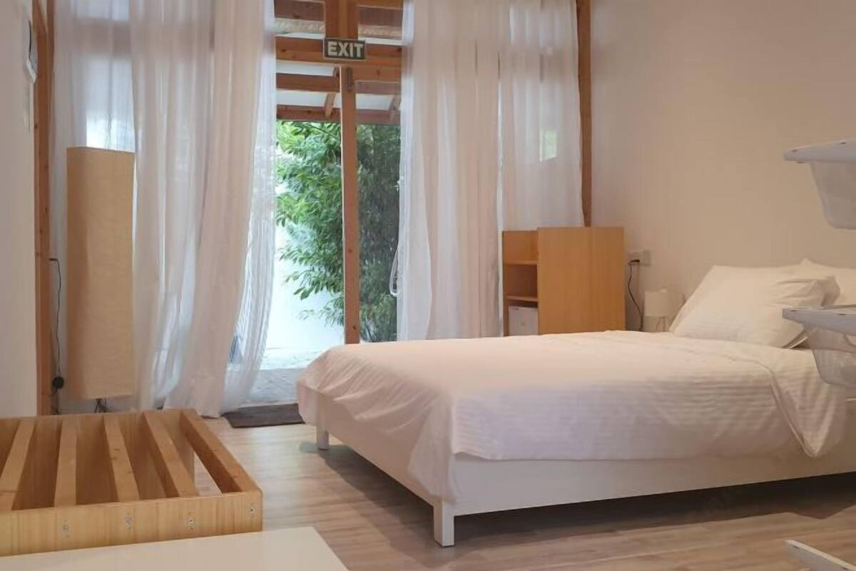 Un dormitorio con cama, una mesita de noche de madera y una ventana con cortinas.