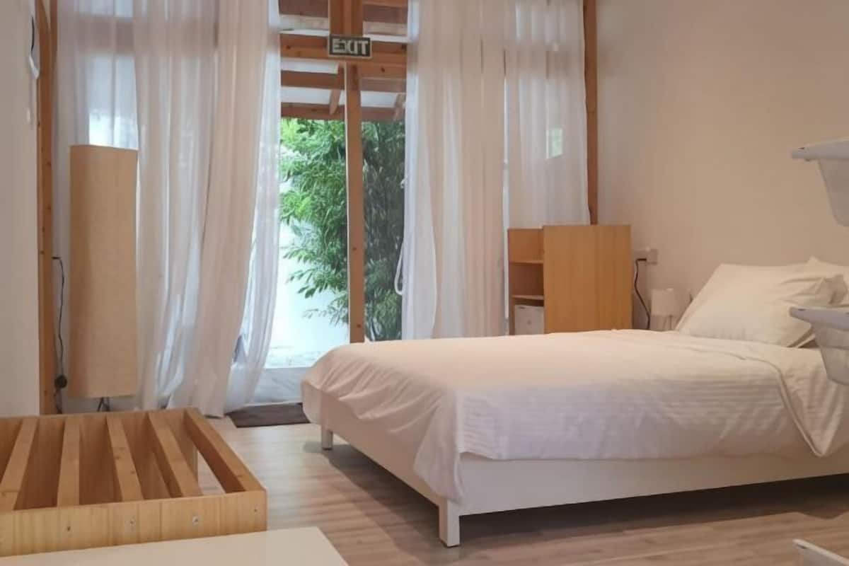 Un dormitorio con cama, una mesita de noche de madera y una ventana con cortinas.