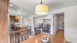 A modern kitchen with wooden cabinets, a dining table with chairs, and a central island. - Charming 4-Bedroom Home, Short Walk to Lambeau (Green Bay)