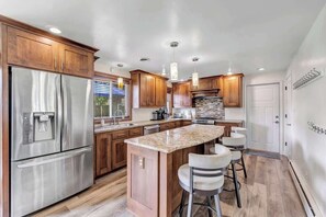 A modern kitchen with wooden cabinets, stainless steel appliances, and a central island with bar stools. - Charming 4-Bedroom Home, Short Walk to Lambeau (Green Bay)