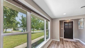 A spacious hallway with large windows, a wooden floor, and a door leading to another room. - Charming 4-Bedroom Home, Short Walk to Lambeau (Green Bay)