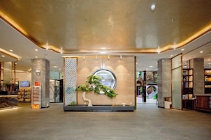 Un vestíbulo amplio con una recepción, un adorno circular grande en la pared y un arreglo de plantas.