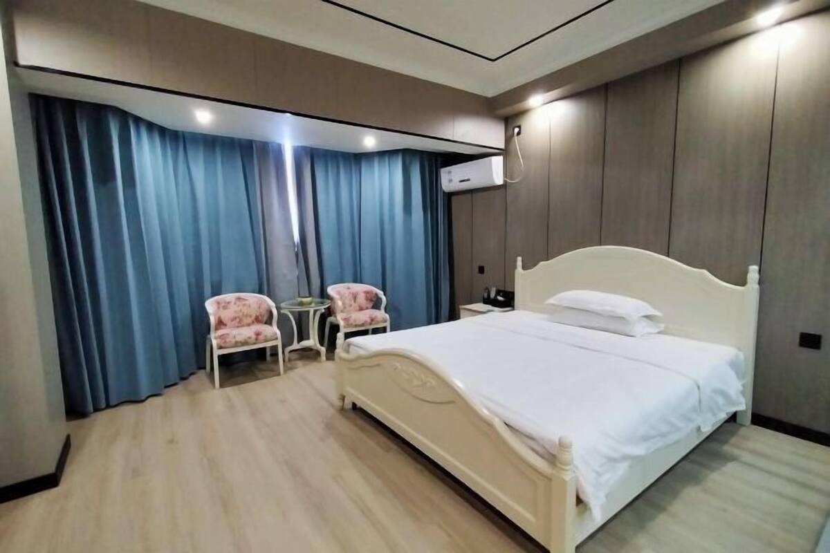 A bedroom with a bed, two chairs, a small table, and a wall-mounted air conditioner.
