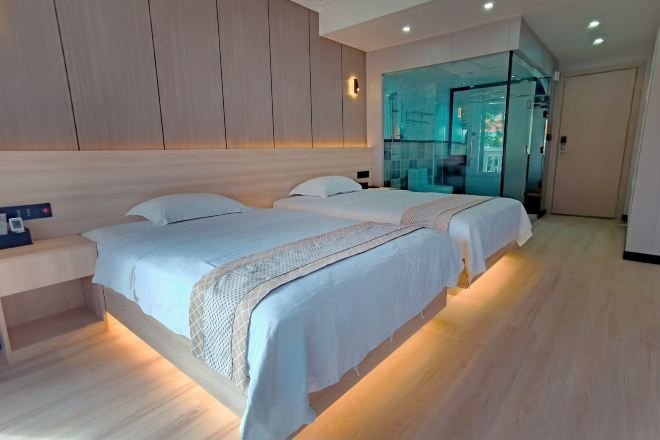A modern bedroom with two beds, a bedside table, and a glass partition wall.