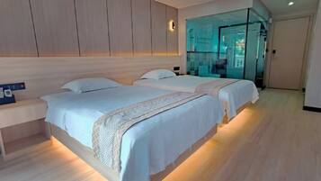 A modern bedroom with two beds, a bedside table, and a glass partition wall.